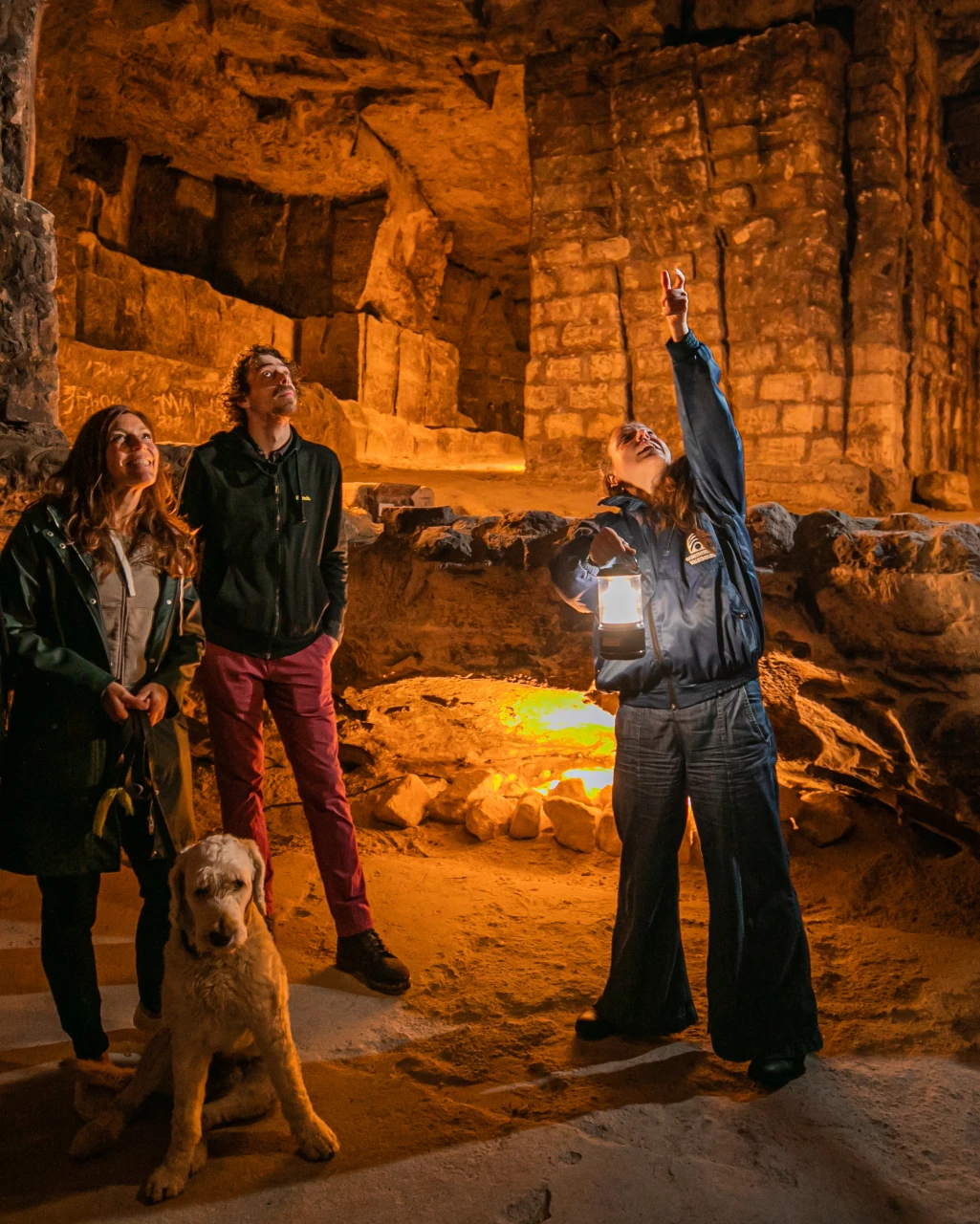 Vrouw die 2 mensen met een huisdier rondleidt in een van de grotten van Valkenburg: de Gemeetegrot